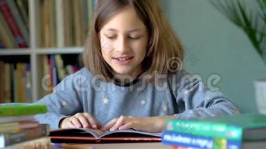 一个微笑的女孩坐在桌子旁，在书中考虑插图。 关闭视野。